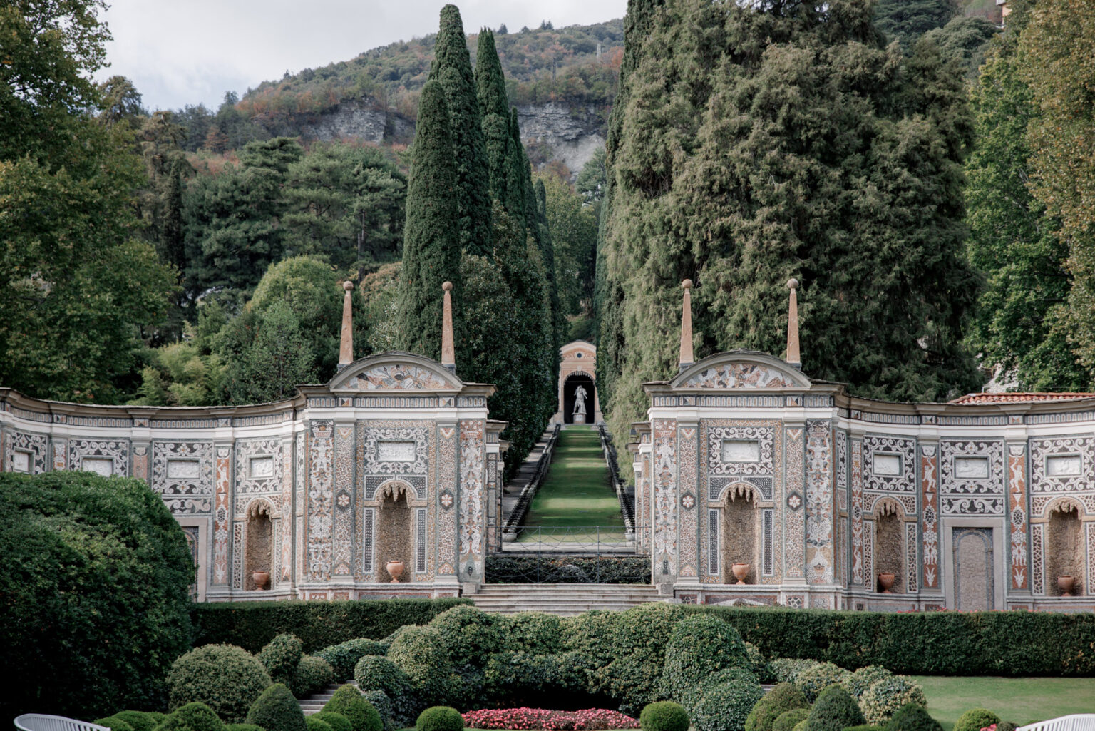 Ein kunstvoll angelegter Garten mit detaillierten Steinmauern, hohen Hecken und üppigem Grün vor der Kulisse eines Hügels - ein idyllisches Ziel, das sich perfekt für Fotografie oder eine Hochzeit im Ausland eignet.
