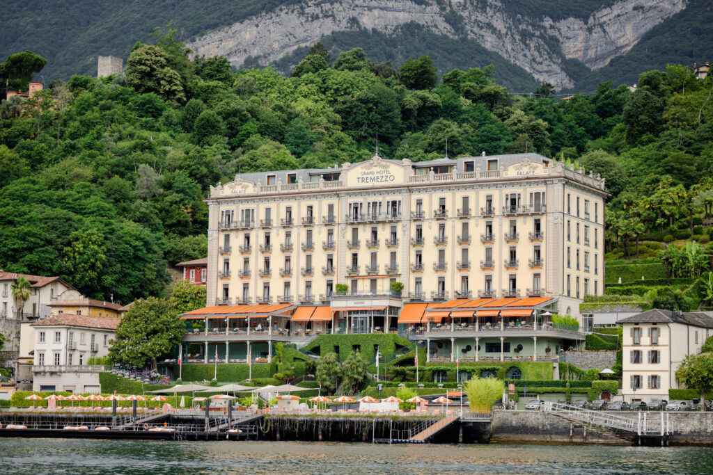 Das Grand Hotel Tremezzo mit seinen orangefarbenen Markisen, umgeben von Grün am Wasser und den Bergen im Hintergrund - ein atemberaubendes Ziel, perfekt für die Fotografie.