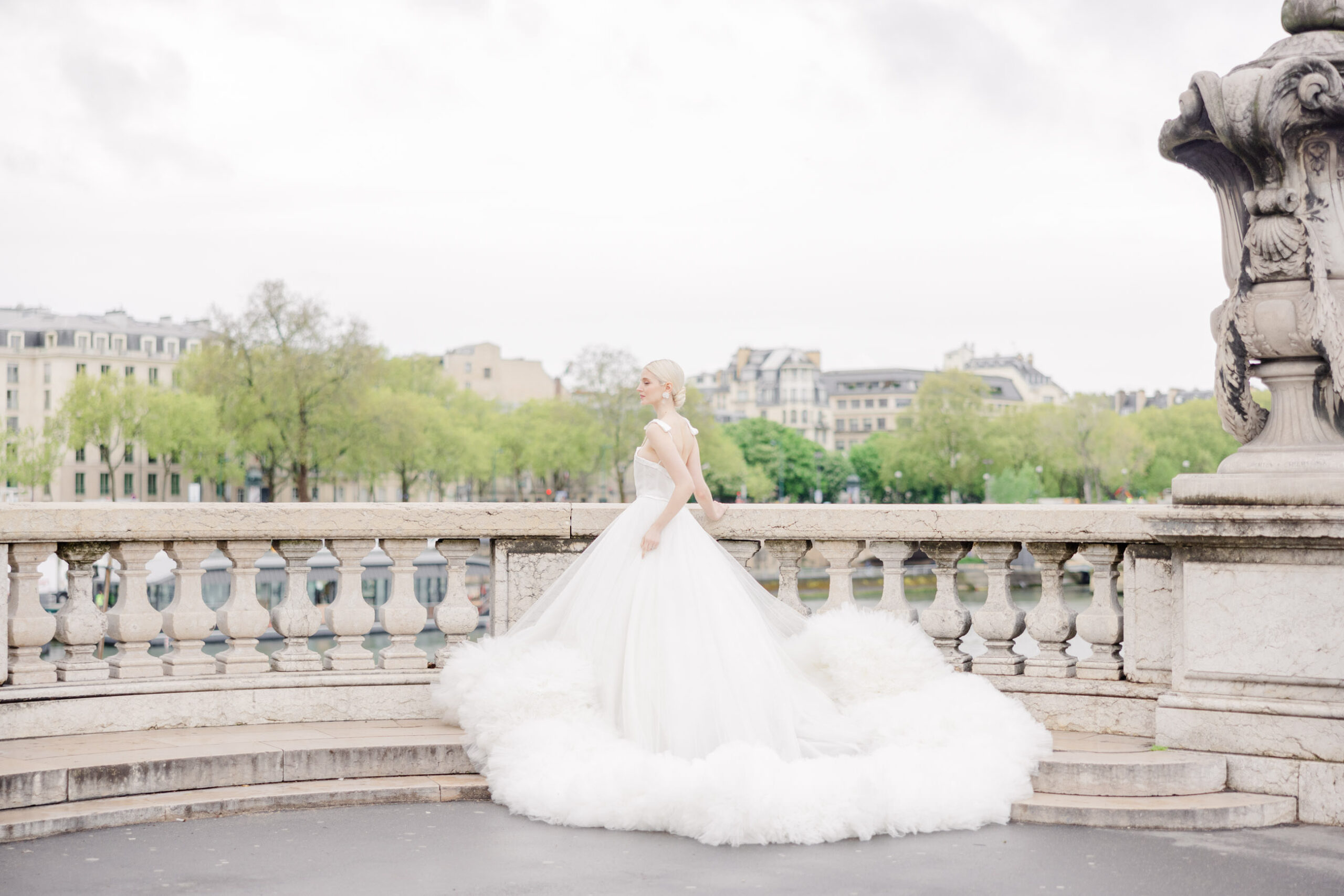 Die Braut im weißen Hochzeitskleid steht auf einer Steinterrasse mit Blick auf die Stadt und den Fluss und fängt den Zauber einer Hochzeit im Ausland in dieser atemberaubenden Fotografie ein.