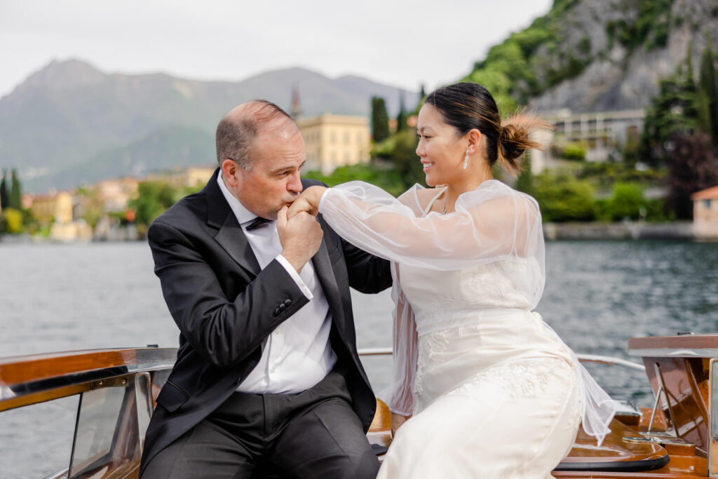 Ein Mann im Anzug küsst die Hand einer Frau, während sie lächelnd auf einem Boot sitzen, umgeben von Bergen und Wasser - das perfekte filmreife Ziel für einen Hauch von Luxus.