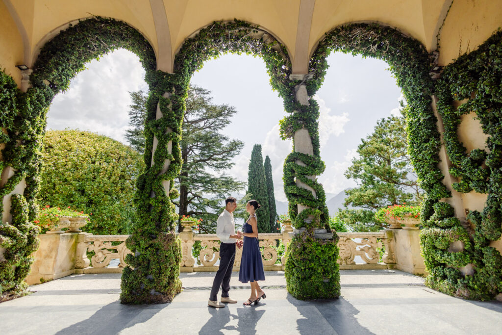 Ein Paar steht sich unter einem efeubewachsenen Torbogen gegenüber, mit einem malerischen Garten im Hintergrund - das perfekte Ziel für eine Luxus-Hochzeit im Ausland.