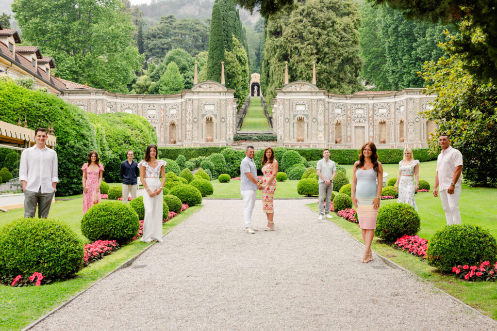 Eine Gruppe von Menschen posiert in einem formalen Garten mit kunstvoller Architektur und üppigem Grün, der die Essenz eines Luxusreiseziels einfängt, das sich perfekt für eine Hochzeit im Ausland eignet.