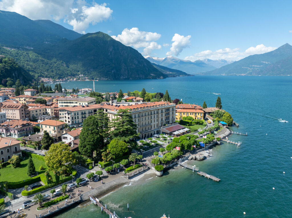 Die 10 schönsten Hochzeitslocations am Comer See 18 Luftaufnahme eines Reiseziels am See mit Bergen, bunten Gebäuden und einer Uferpromenade, eingefangen in einer atemberaubenden Fotografie.