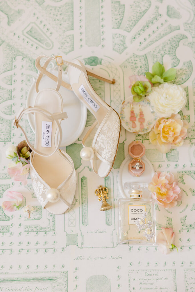 Elegant bridal shoes, Chanel perfume, flowers, and jewelry, arranged on a decorative green-and-white background—the perfect photography for an unforgettable destination wedding.