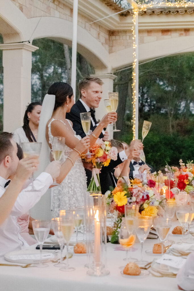 Braut und Bräutigam stoßen auf einer eleganten, blumengeschmückten Hochzeitsfeier im Freien mit Champagner an.