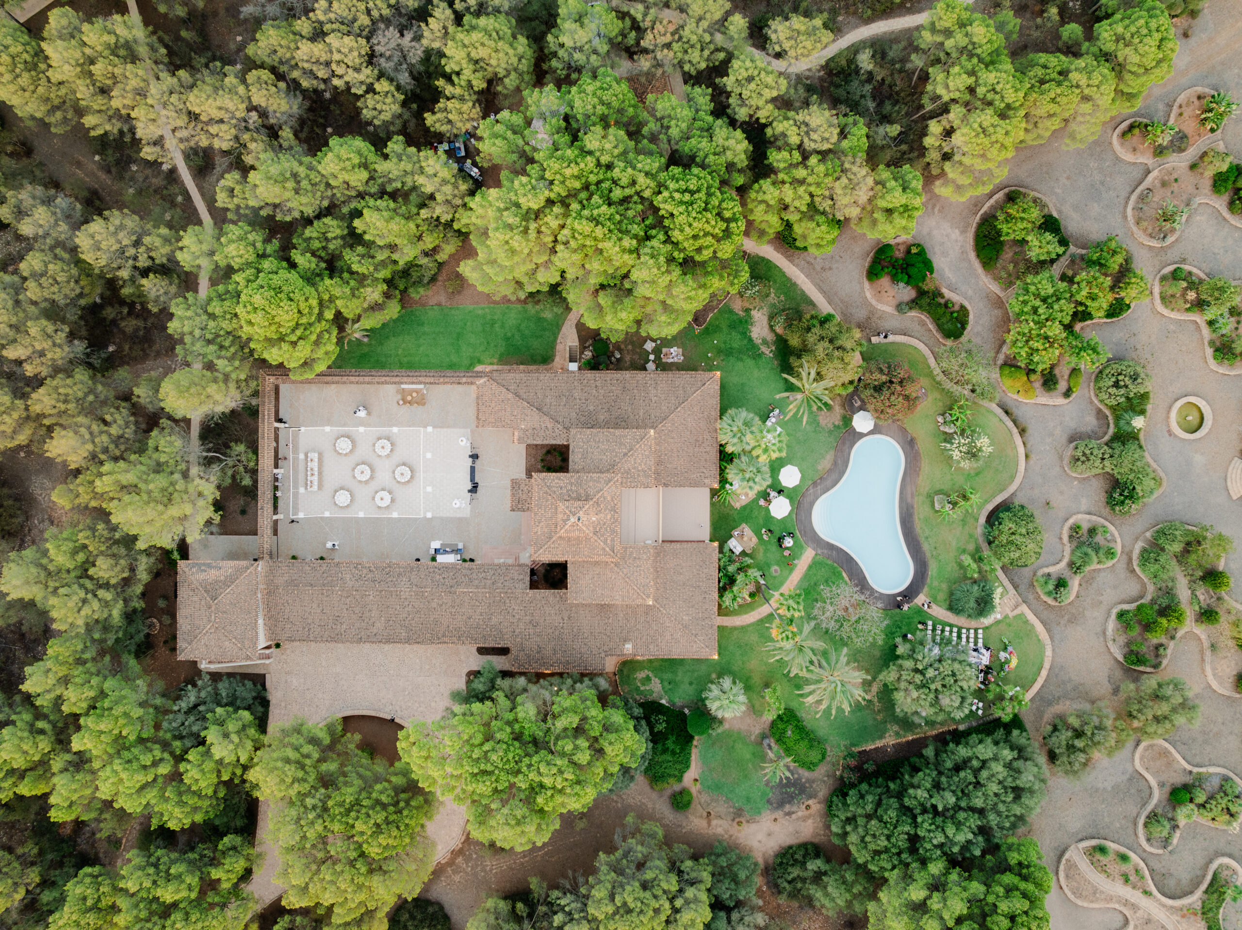 Luftaufnahme eines großen Hauses mit Innenhof, Pool und Garten, umgeben von dichten grünen Bäumen.