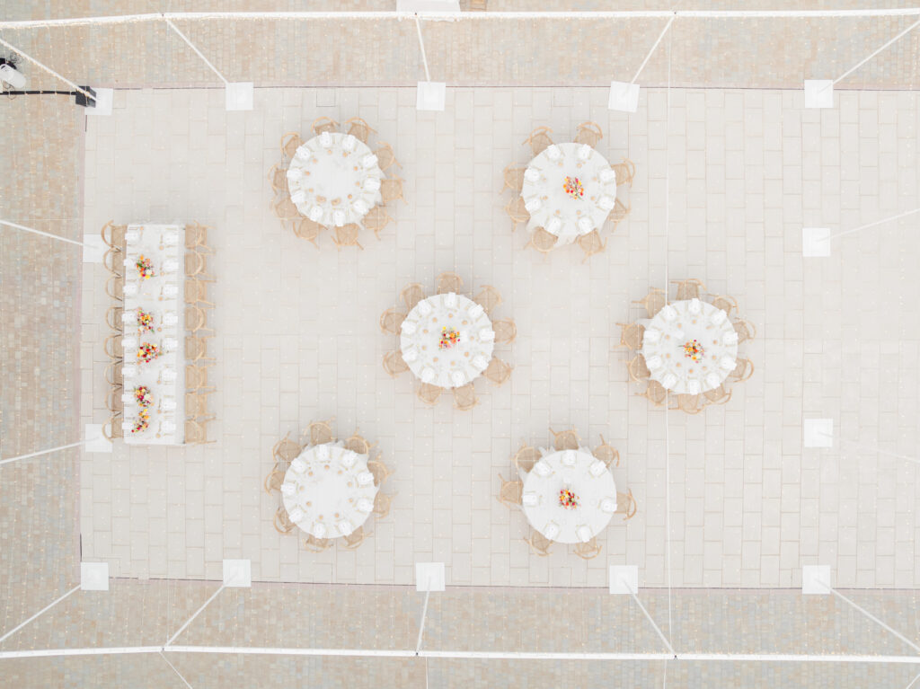 Luftaufnahme von runden Tischen, die für eine Veranstaltung im Freien gedeckt sind, mit einem langen rechteckigen Tisch auf der linken Seite.