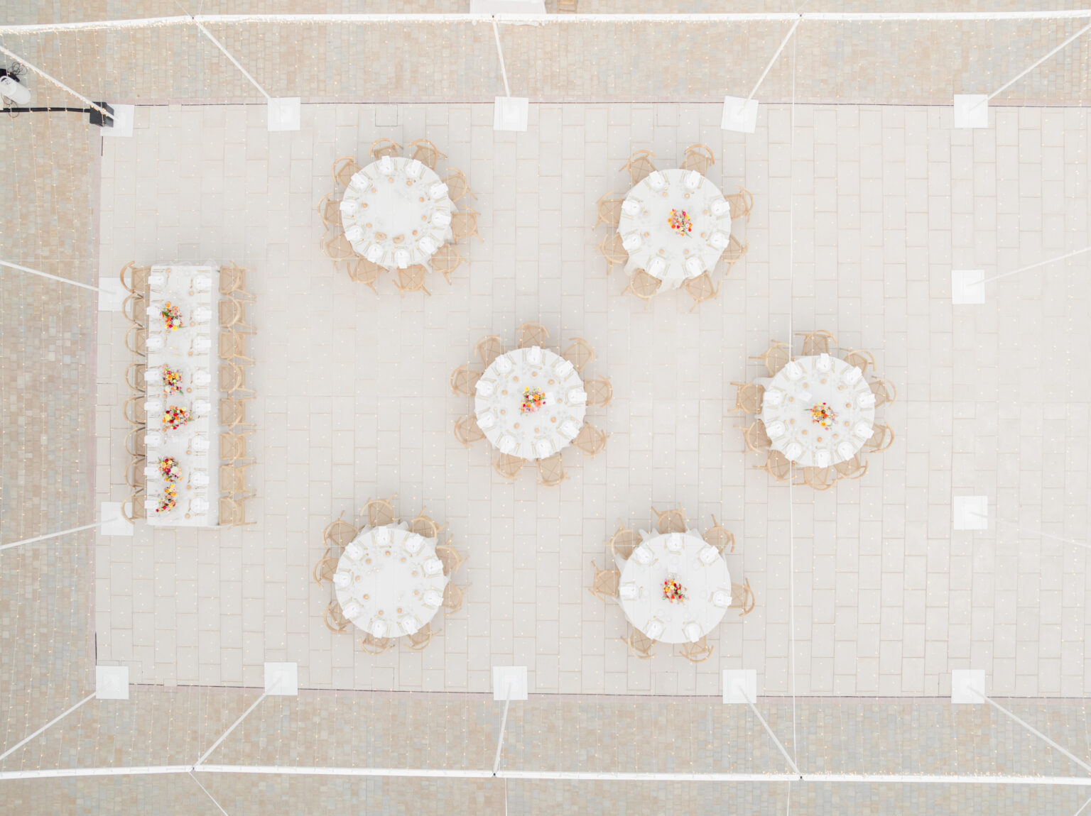 Wedding Photography Mallorca 18 Luftaufnahme von runden Tischen, die für eine Veranstaltung im Freien gedeckt sind, mit einem langen rechteckigen Tisch auf der linken Seite.