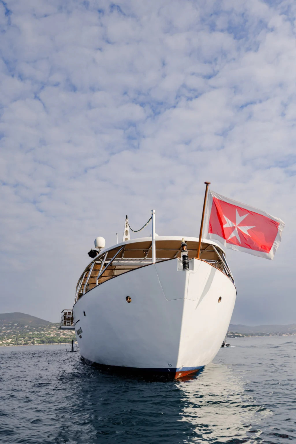 Wedding Photography South France 17 Eine weiße Yacht auf dem Wasser, die eine rote Flagge mit einem weißen Malteserkreuz führt.
