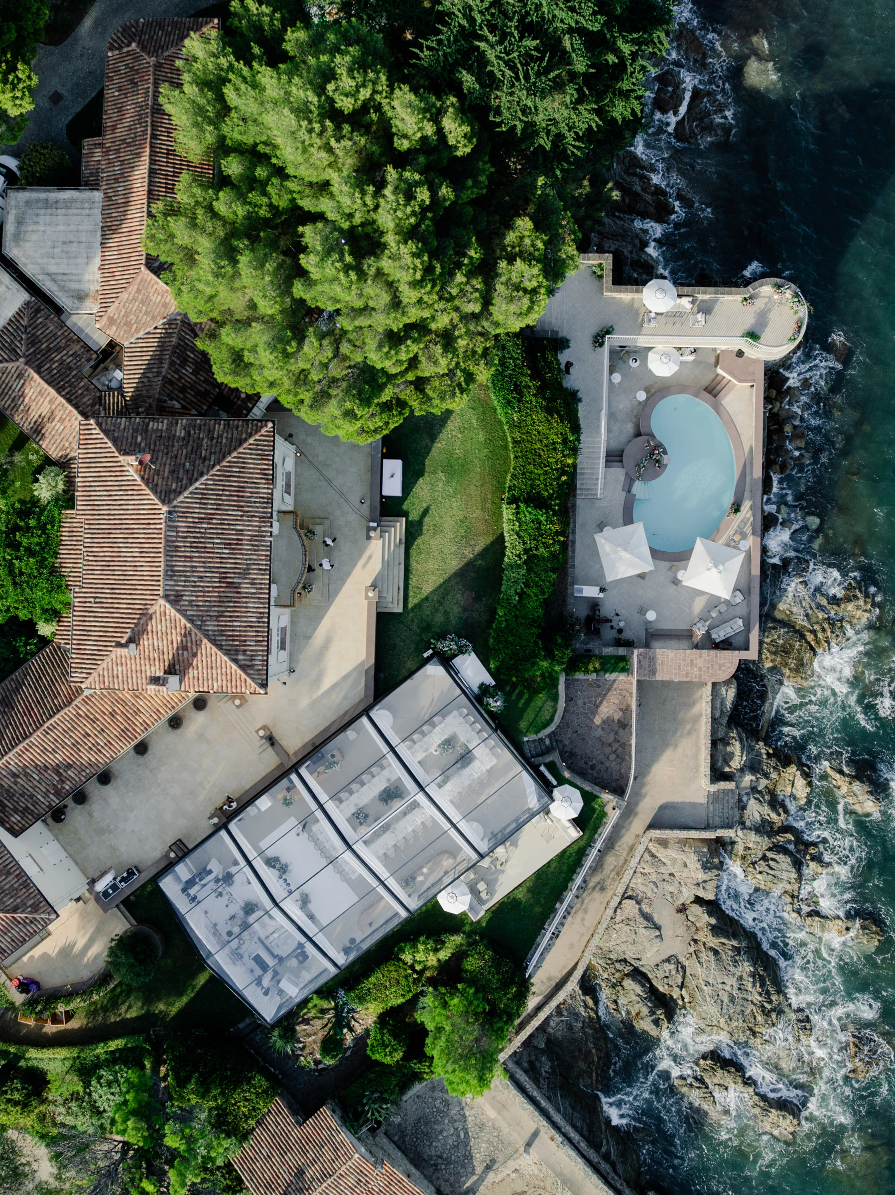 Luftaufnahme einer Villa an der Küste mit Swimmingpool und einem großen Zelt im Außenbereich.