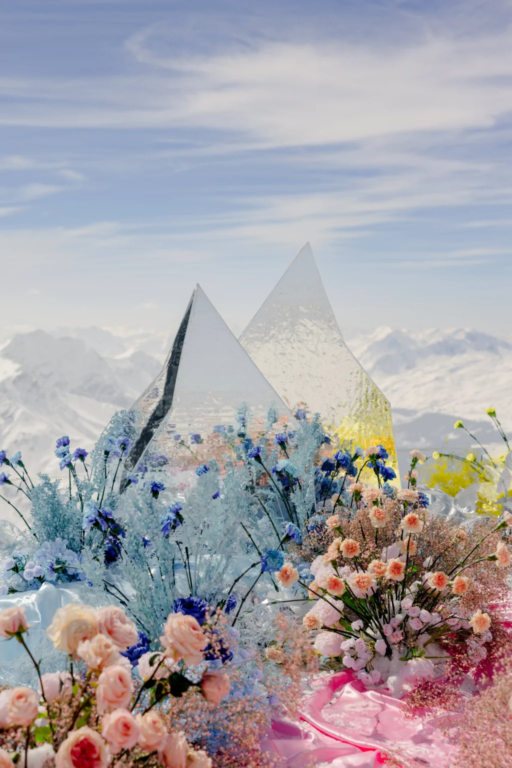 Flower arrangement with two triangular ice sculptures in front of a snowy mountain range.