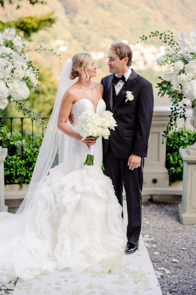 Hochzeitslocation Relais Villa Vittoria am Comer See – Intime Hochzeit in einer historischen Villa 14 Die Braut in einem weißen Brautkleid und der Bräutigam in einem schwarzen Smoking blicken sich im Relais Villa Vittoria an.