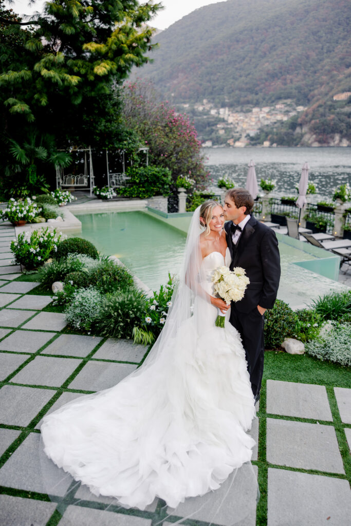 Hochzeitslocation Relais Villa Vittoria am Comer See – Intime Hochzeit in einer historischen Villa 1 Ein Brautpaar posiert am Swimmingpool der Relais Villa Vittoria mit Blick auf einen See.