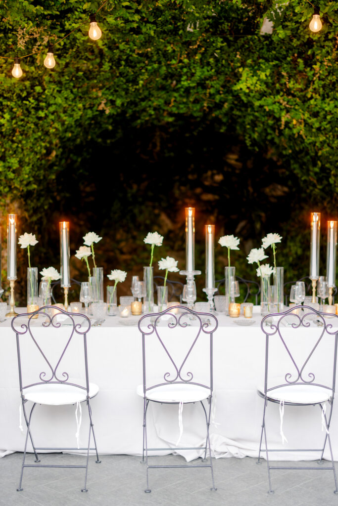Hochzeitslocation Relais Villa Vittoria am Comer See – Intime Hochzeit in einer historischen Villa 19 Ein langer Tisch im Relais Villa Vittoria, gedeckt für das Abendessen, mit weißen Blumen und brennenden Kerzen inmitten von Grün.
