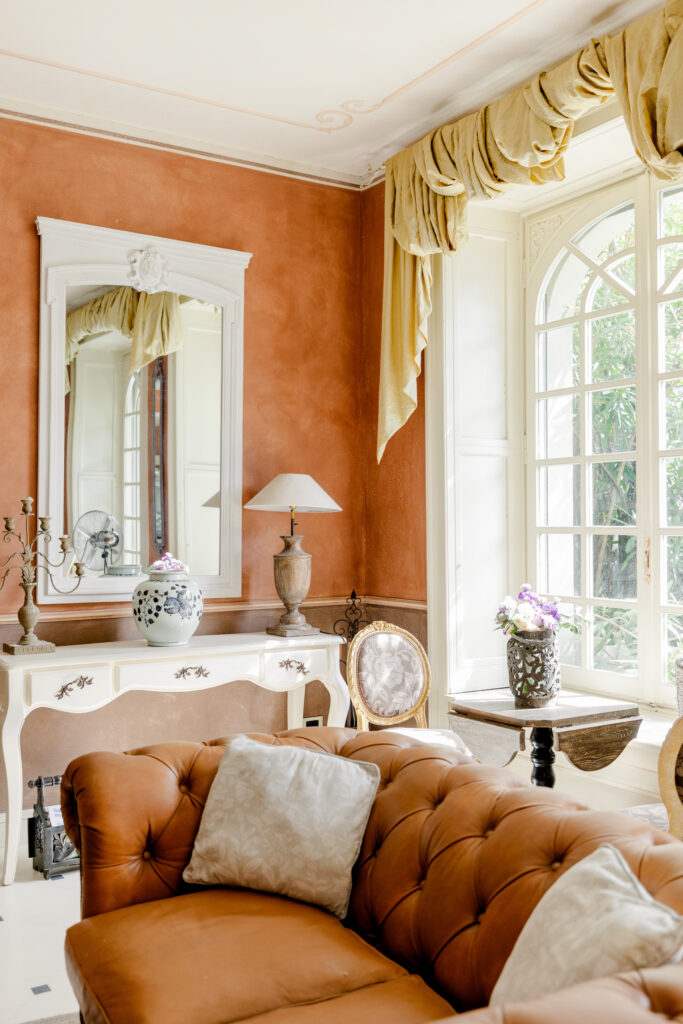 Hochzeitslocation Relais Villa Vittoria am Comer See – Intime Hochzeit in einer historischen Villa 3 Das Wohnzimmer im Relais Villa Vittoria mit einem hellbraunen Ledersofa, einem weißen Konsolentisch, einem Spiegel und einem Fenster.