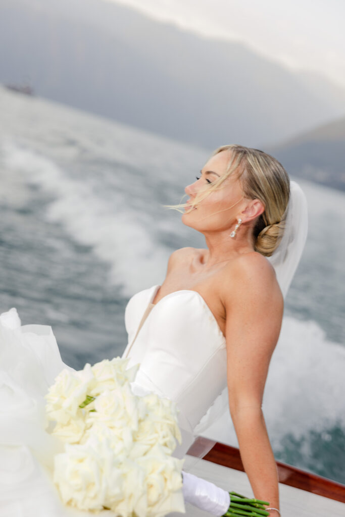 Hochzeitslocation Relais Villa Vittoria am Comer See – Intime Hochzeit in einer historischen Villa 7 Eine Braut in einem weißen Brautkleid, die weiße Rosen in den Händen hält, während sie im Relais Villa Vittoria eine Bootsfahrt unternimmt.