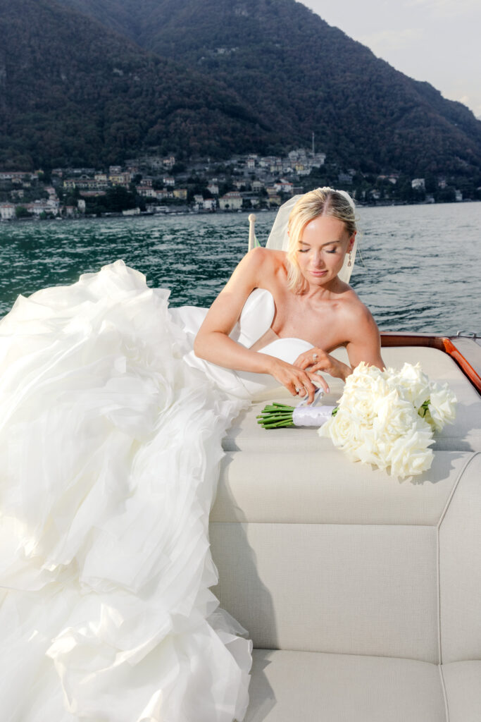 Hochzeitslocation Relais Villa Vittoria am Comer See – Intime Hochzeit in einer historischen Villa 4 Eine Braut in einem weißen Hochzeitskleid liegt auf einem Boot im Relais Villa Vittoria, umgeben von weißen Rosen.